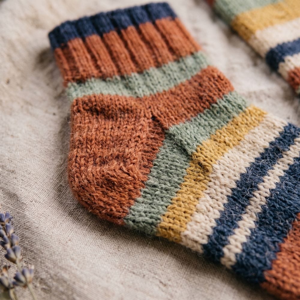 A close-up photo of a pair of striped wool socks in rust, mustard and green