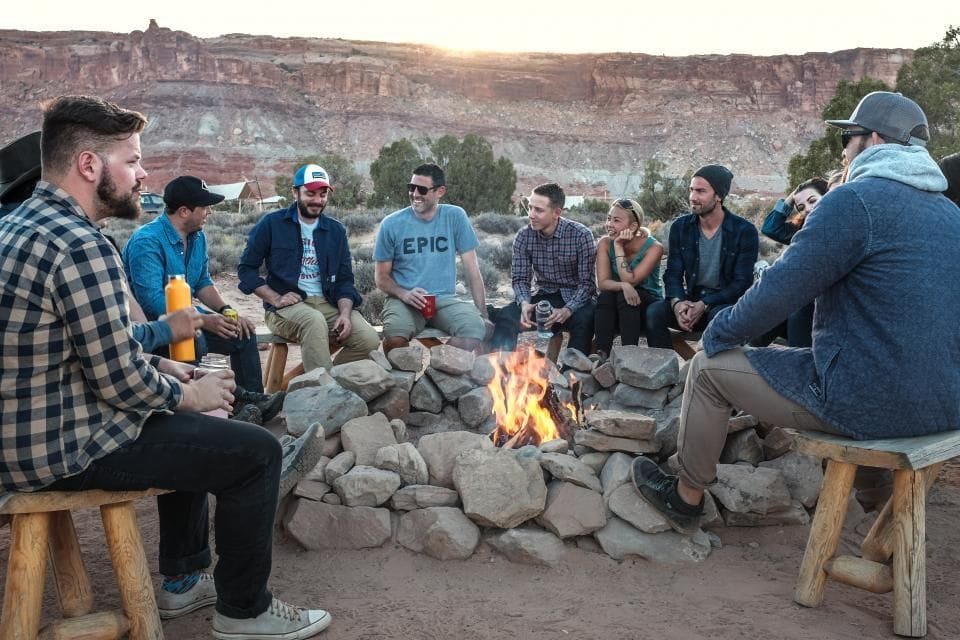 A group sitting on logs around a campfire at dusk