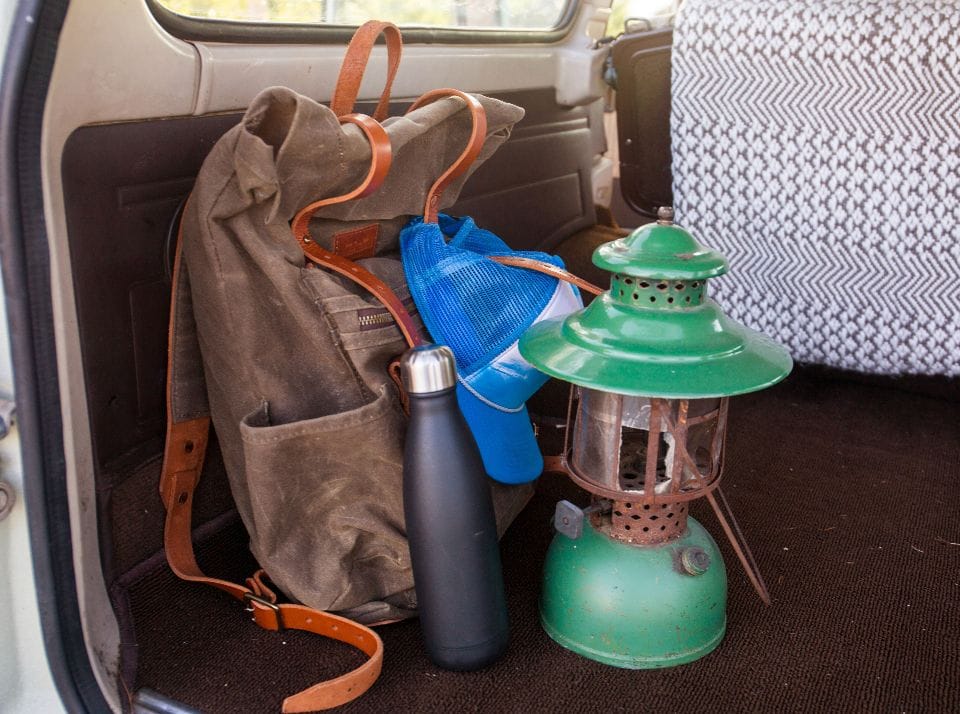 A canvas backpack, a lantern and a water bottle in the back of a car
