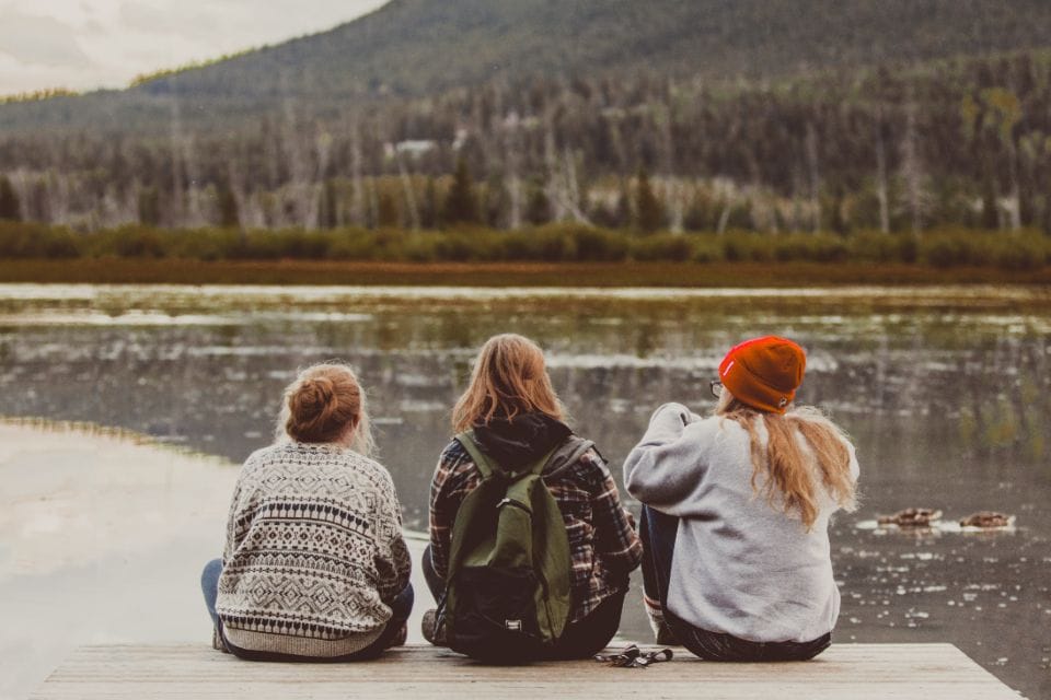 Three friends sitting by a lake looking at the hills