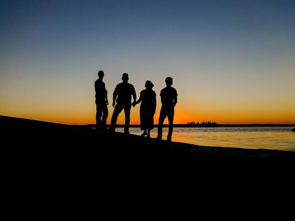 Four friends standing on a hill, silhouetted against the sunset