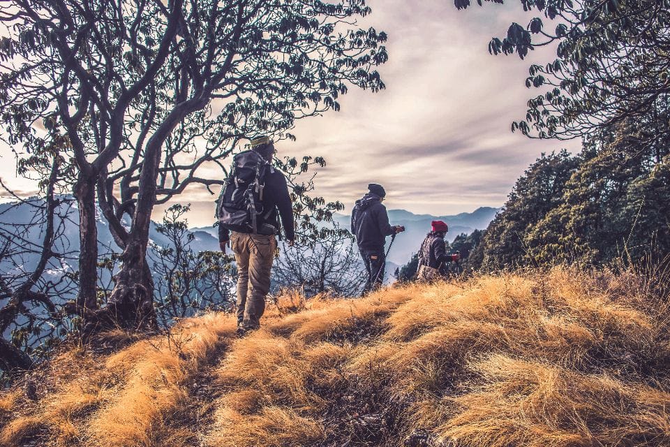 Three hikers with backpacks climbing a grassy ridge in autumn light