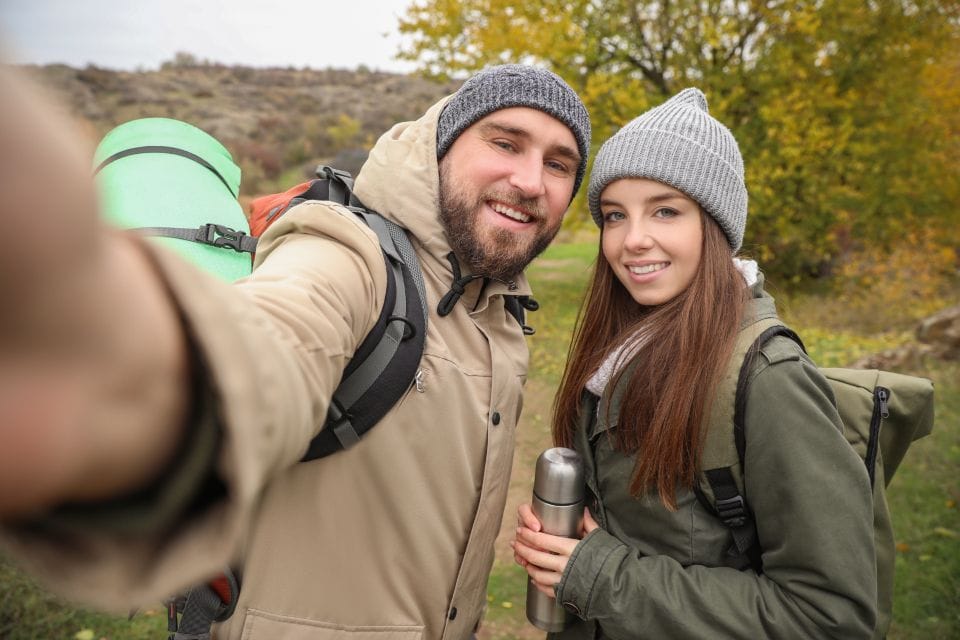 Two smiling hikers in knit hats taking a selfie on the trail