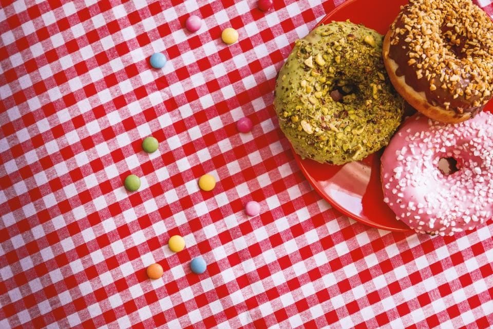 Three glazed donuts on a red and white checked tablecloth