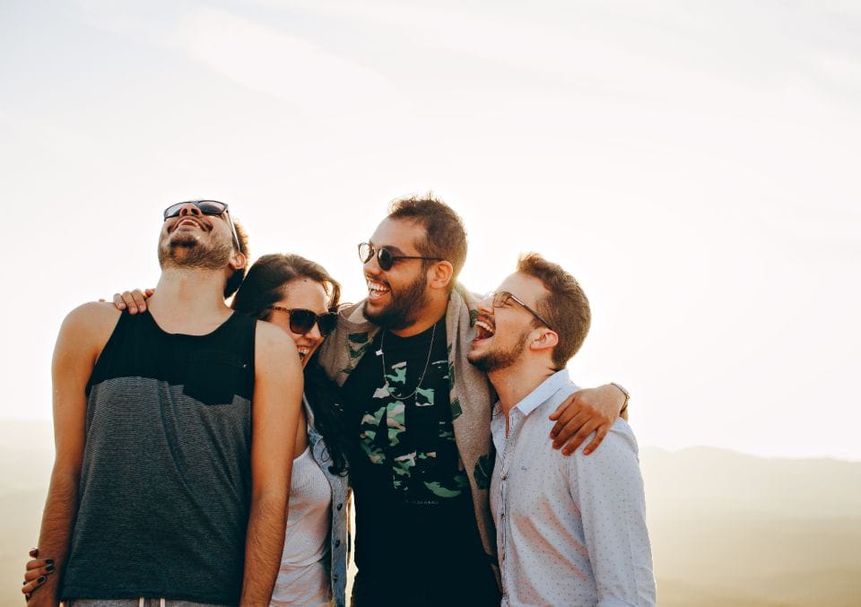 Three friends in sunglasses laughing together outdoors