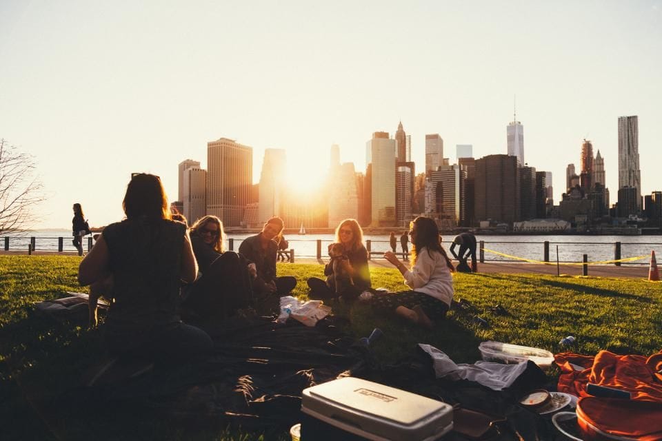 People on picnic blankets watching the sun set behind the city skyline