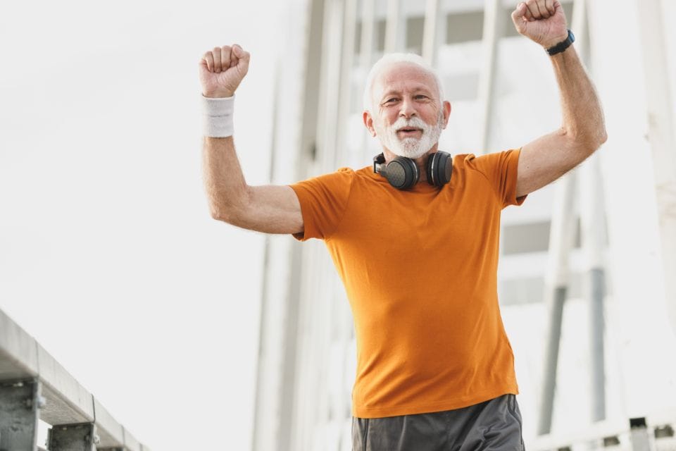 An older runner in an orange shirt cheering with both fists up
