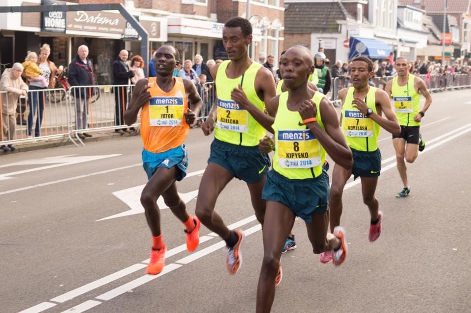 A pack of runners in bright vests racing down a city road