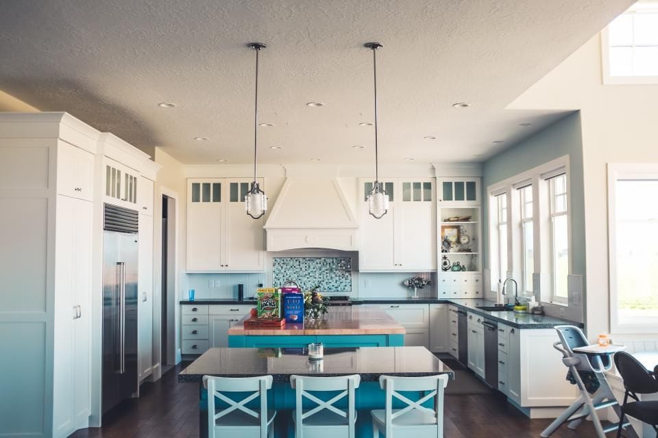 A bright white kitchen with a large island, blue bar stools and pendant lights
