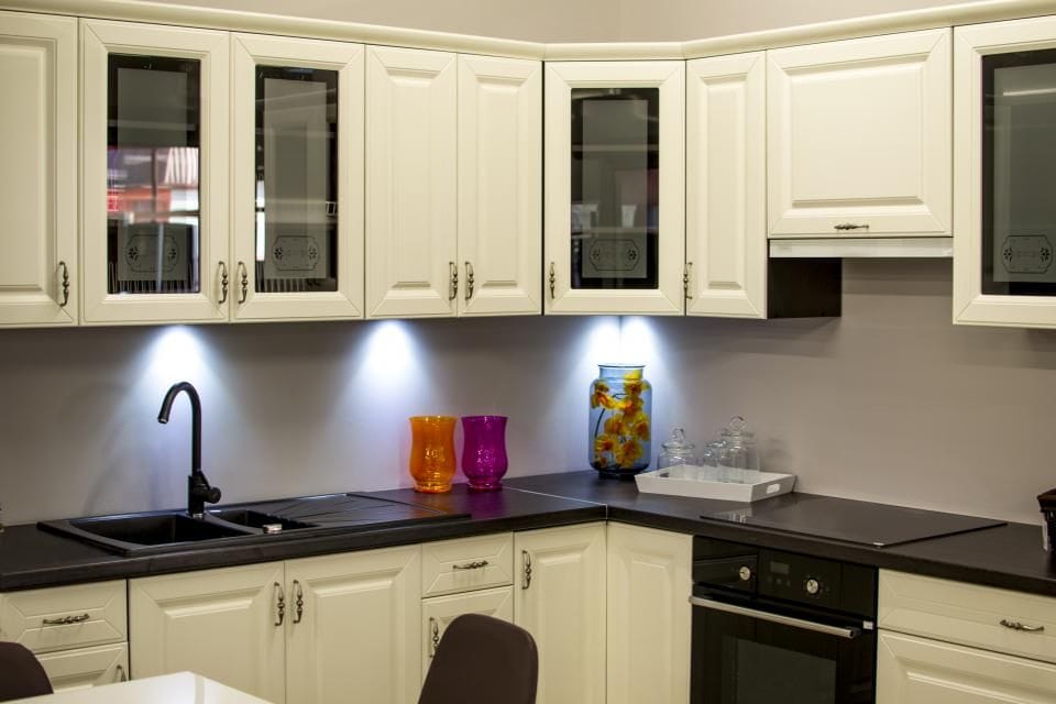 Cream cabinets with glass doors and lights underneath a dark counter