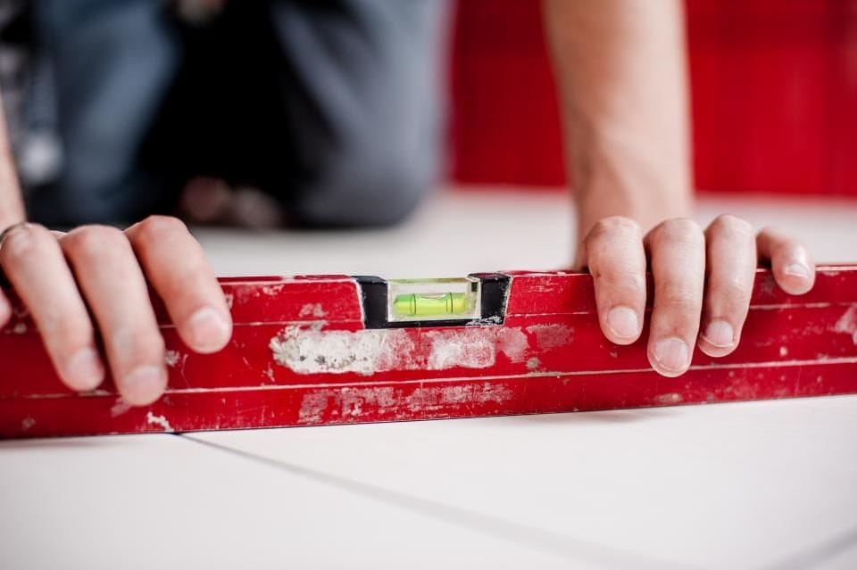 Two hands holding a red spirit level against a wall