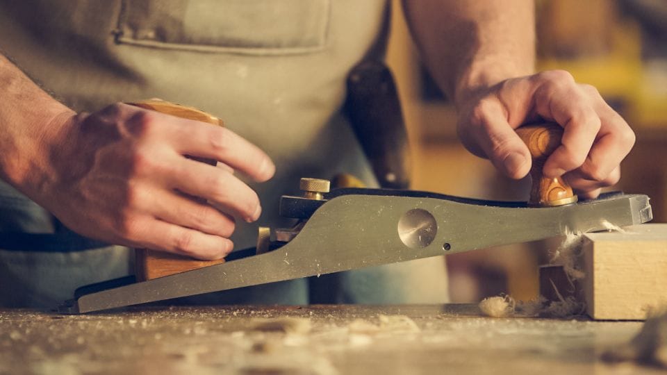 A carpenter planing a piece of wood by hand