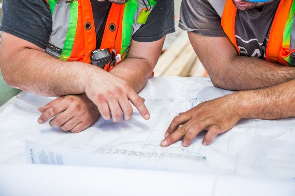 Two builders in safety vests going over drawings on a table