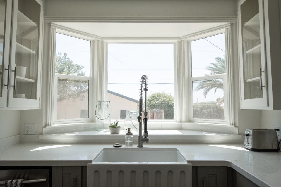 A white farmhouse sink under a wide bay window