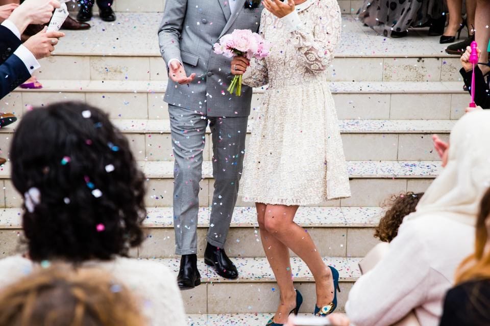 A couple walking down stone steps through falling confetti, guests on either side