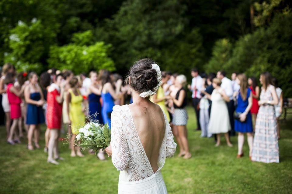 A bride in a lace-back dress among guests at a garden reception