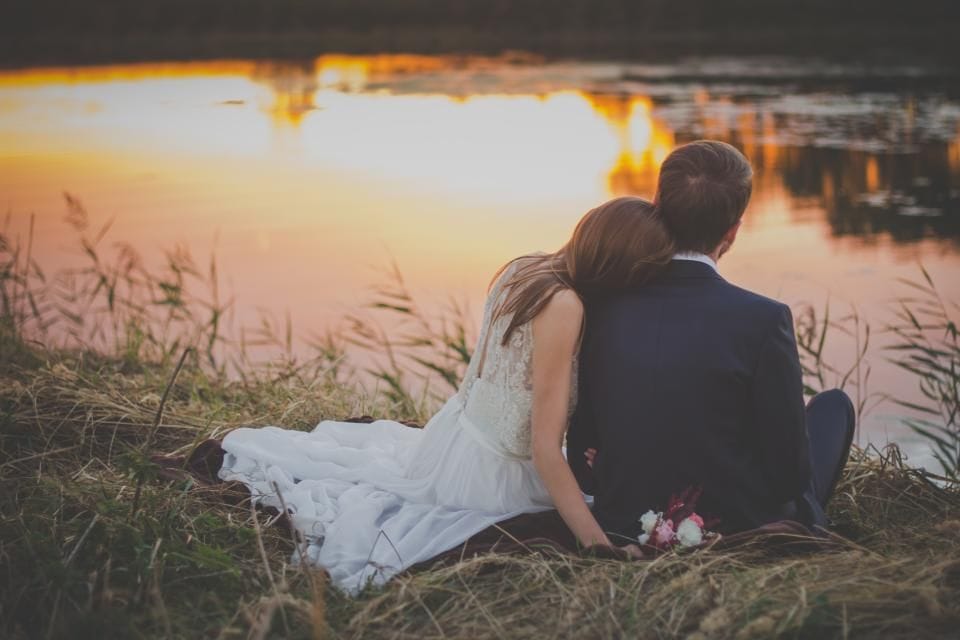 A couple sitting together on the grass by a lake at sunset