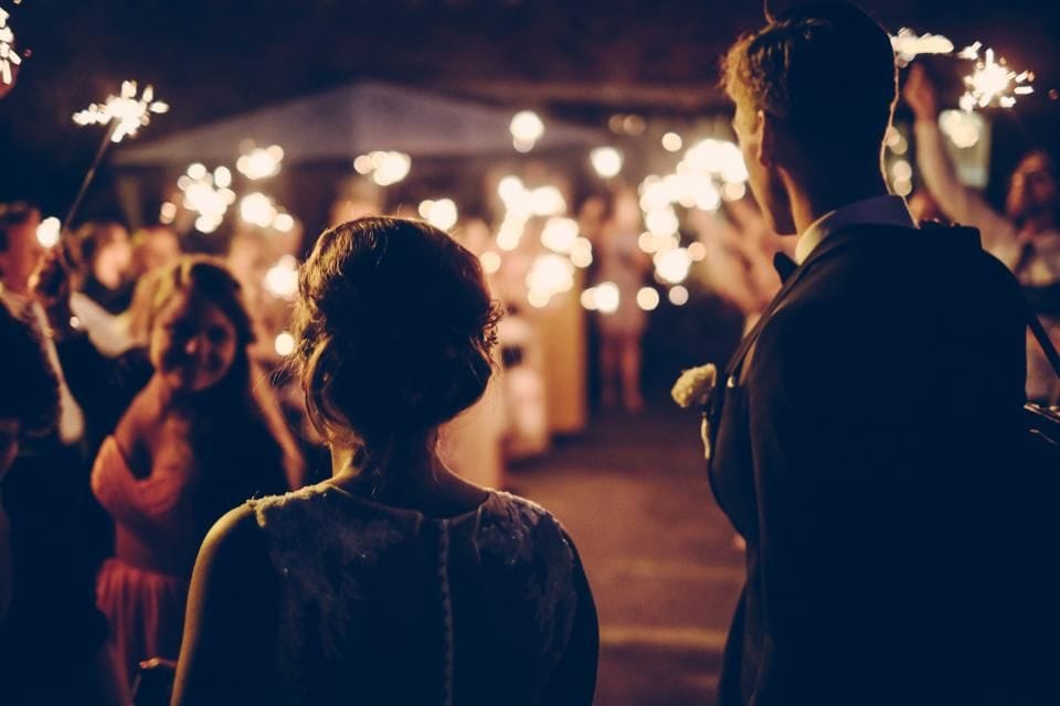Guests holding sparklers at night as a couple walks out through the lights