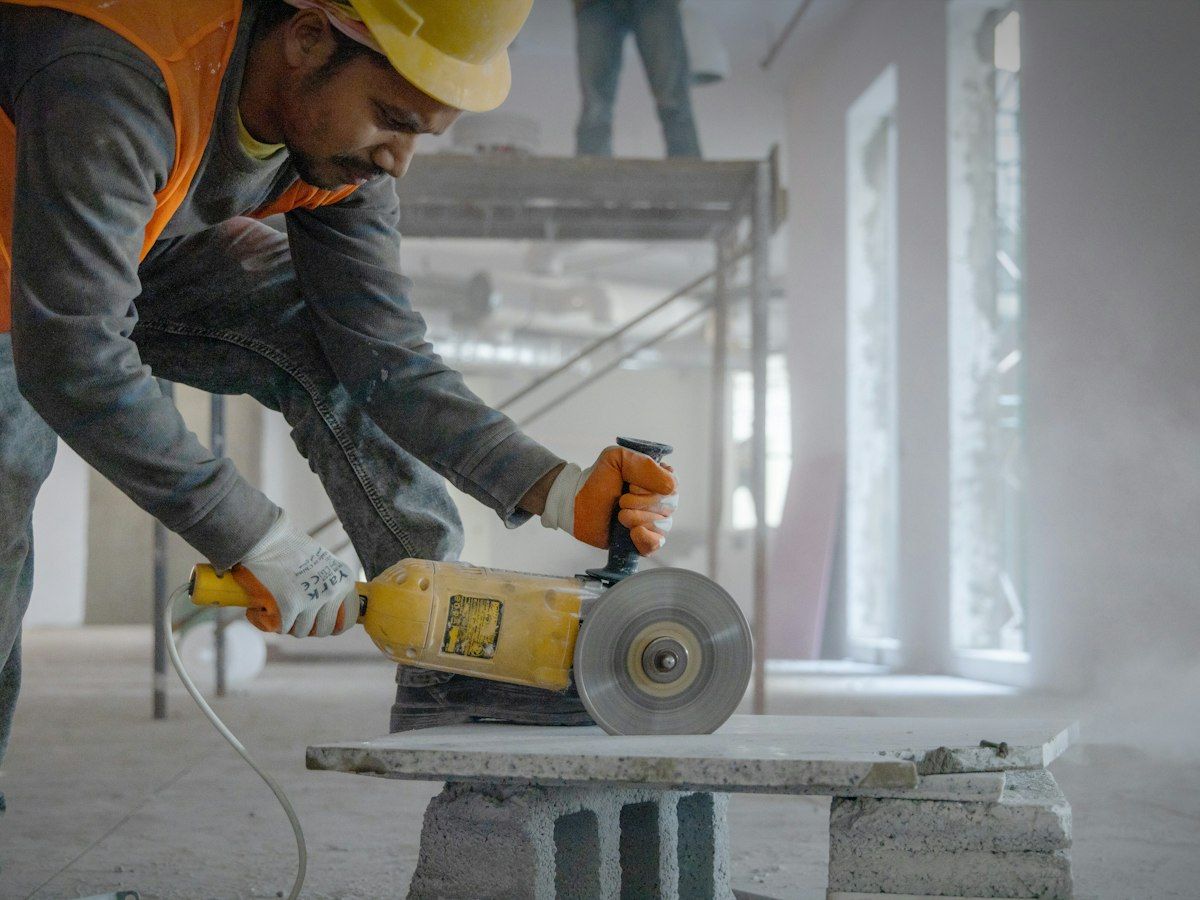 A worker cutting concrete with a grinder, dust in the light
