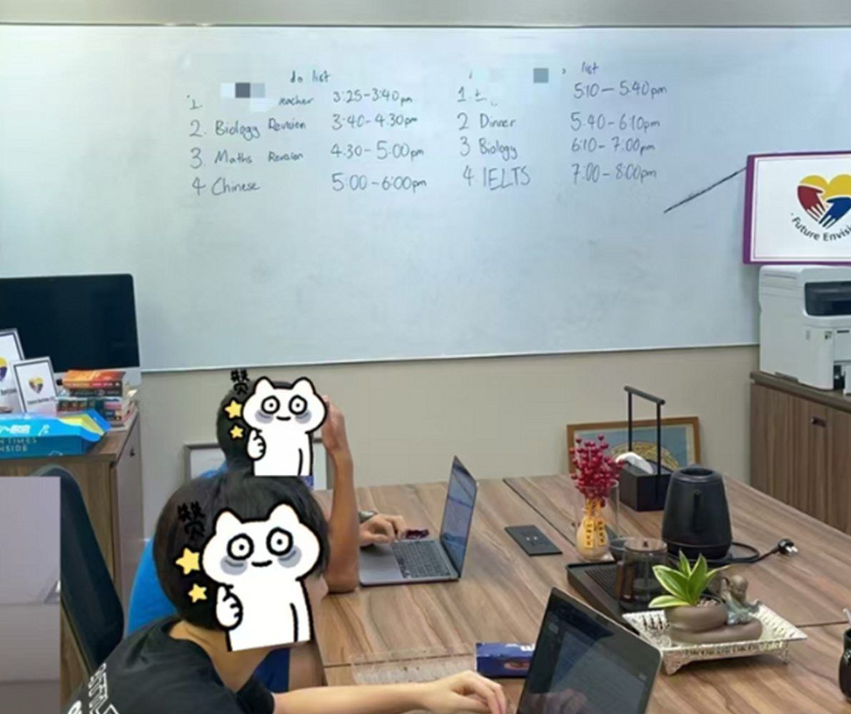 Two students working at laptops in the FE study room, under a whiteboard holding each of their afternoon schedules