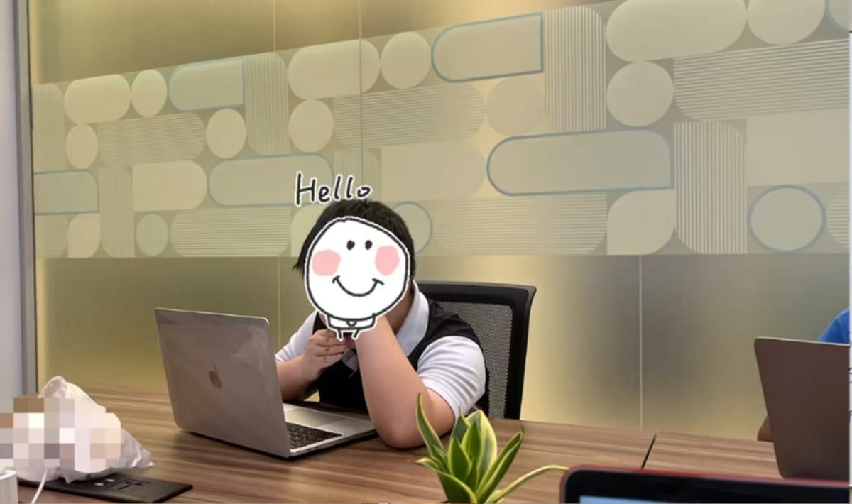 A student at a laptop in the FE study room, in front of a patterned glass wall lettered Hello