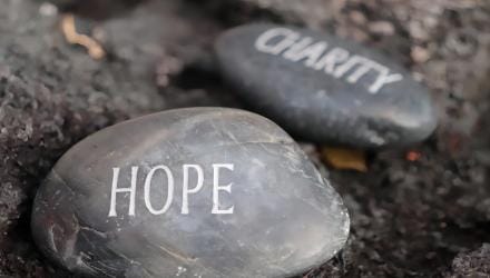 Two smooth stones on dark earth, lettered hope and charity