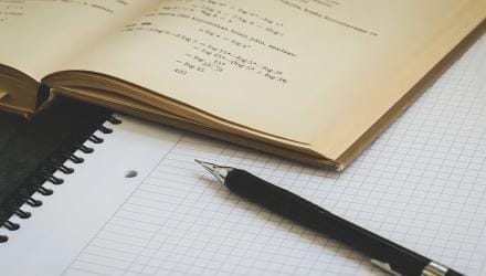 An open maths textbook and a pen resting on squared paper