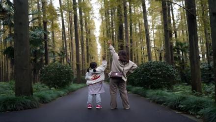 A parent and child walking a forest road, one arm raised toward the trees