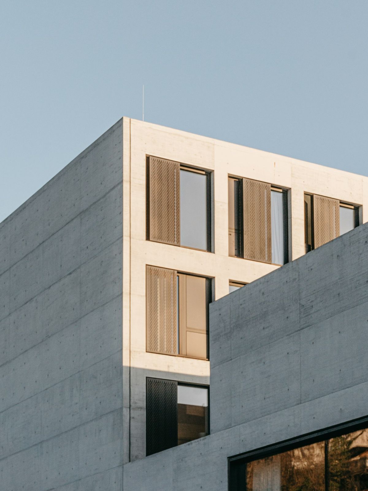 A gray concrete building with timber shutters against a pale sky