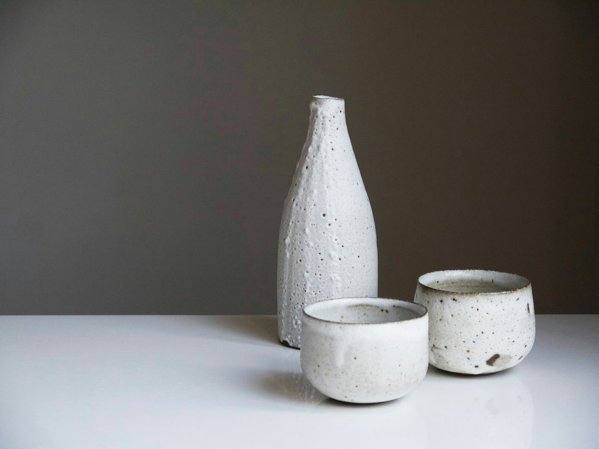 A white stoneware bottle and two small bowls on a gray backdrop