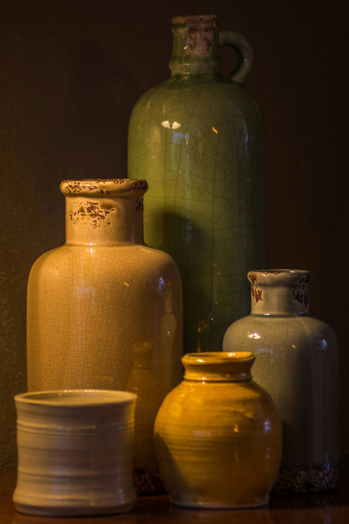 Tall mustard and sage stoneware jars on a dark shelf