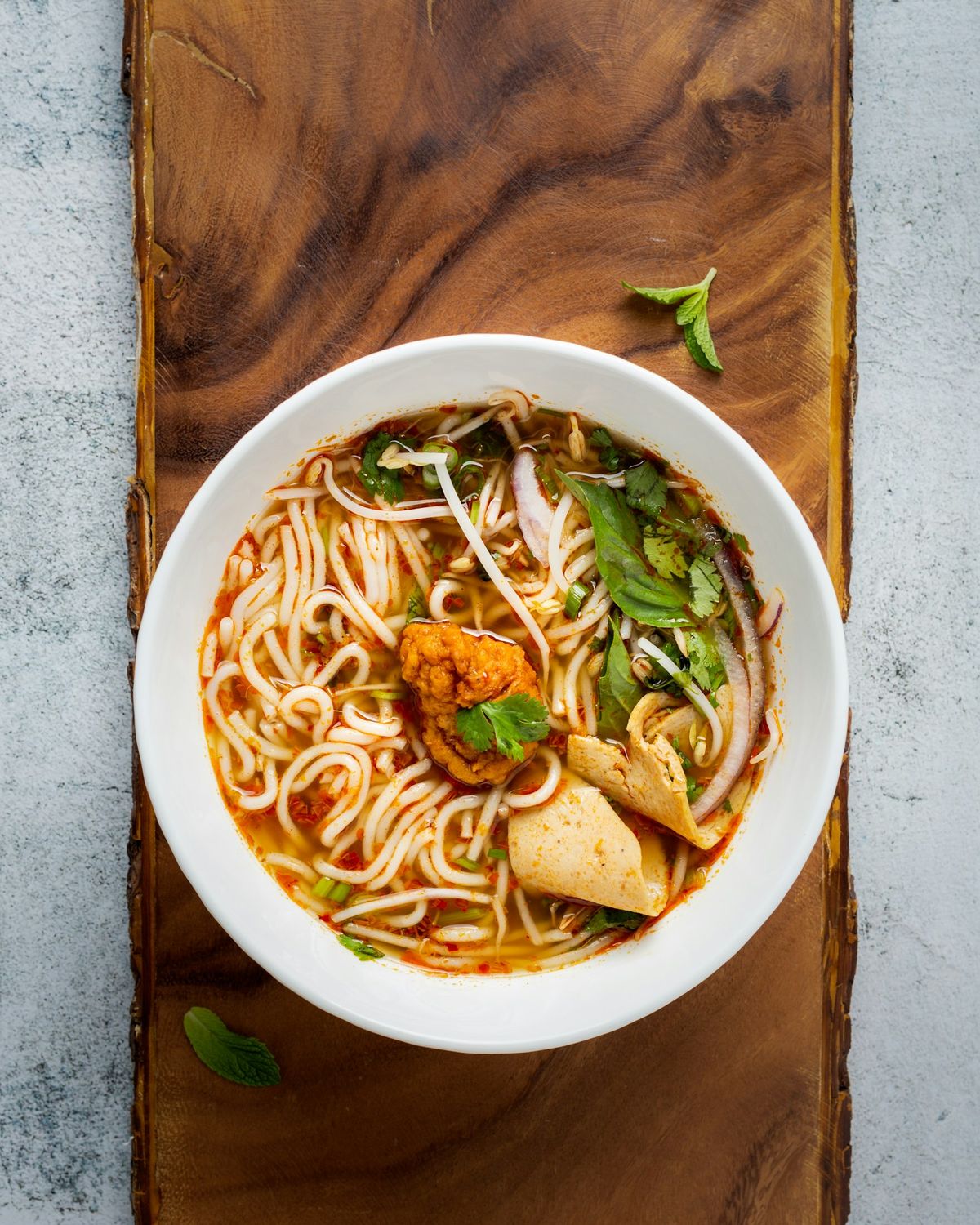 A white bowl of noodles with greens on a wooden board