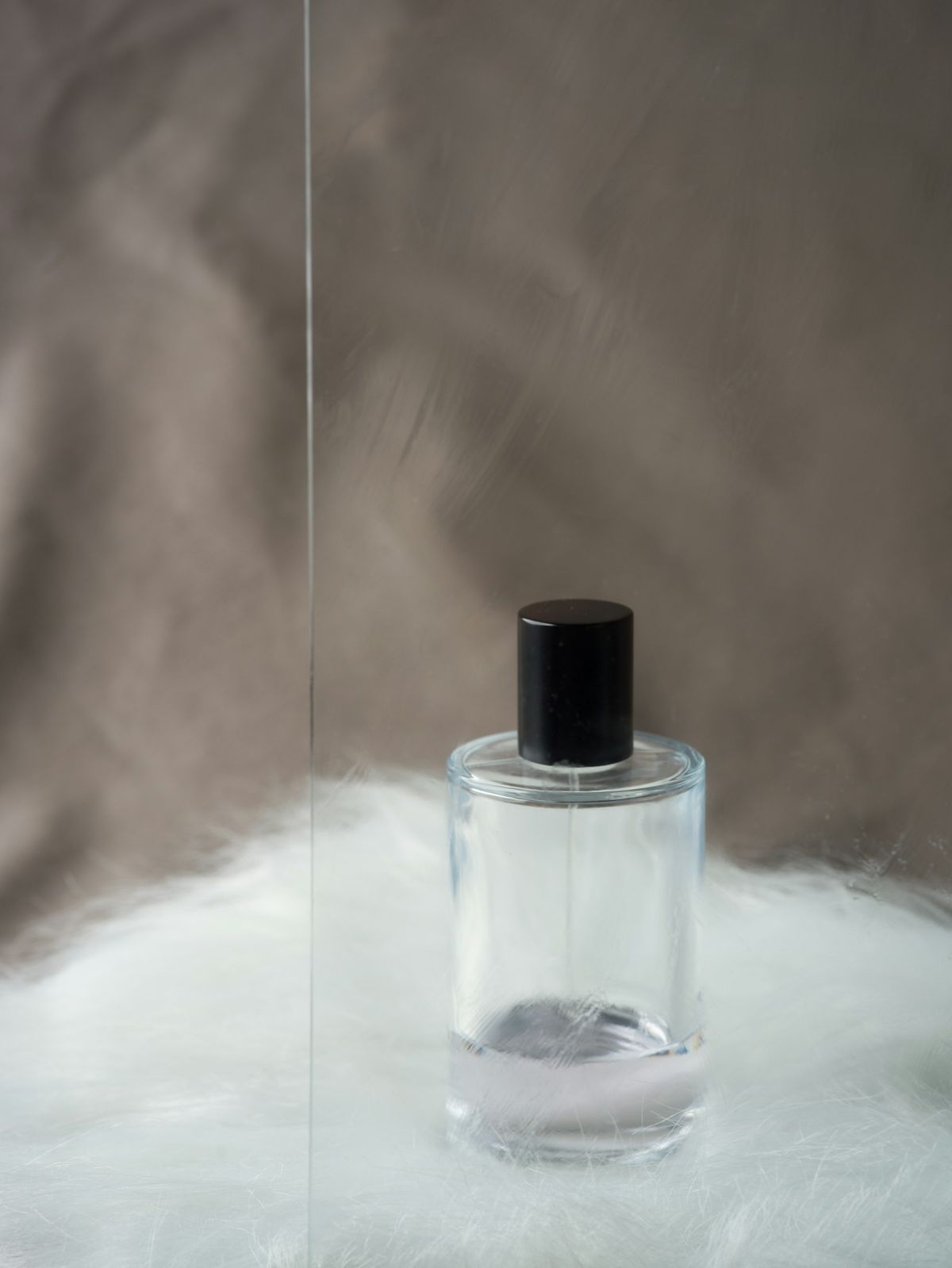 A clear glass bottle with a black cap on soft white fleece