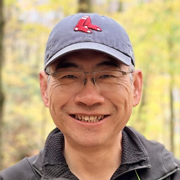 Frank Yang, founder of PageTend, smiling in a Red Sox cap in the autumn woods